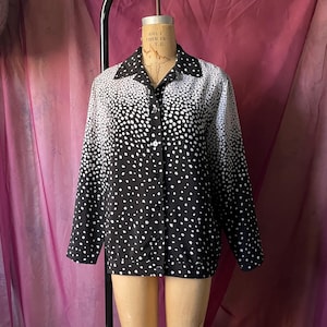 May include: A black button-down shirt with a white polka dot pattern. The polka dots are densely packed at the top and gradually fade towards the bottom. The shirt is displayed on a mannequin.