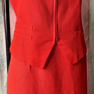May include: A red sleeveless blazer with a zip fastening and two pockets. The blazer is part of a matching skirt suit.