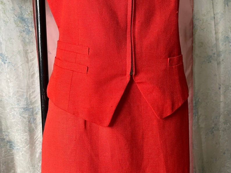 May include: A red sleeveless blazer with a zip fastening and two pockets. The blazer is part of a matching skirt suit.