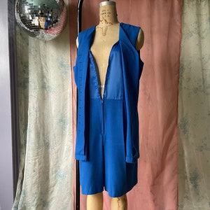 Op de afbeelding: Een koninklijk blauwe, mouwloze jumpsuit met een diepe V-hals en een ritssluiting. De jumpsuit heeft een aansluitend bovenlichaam en wijde pijpen.