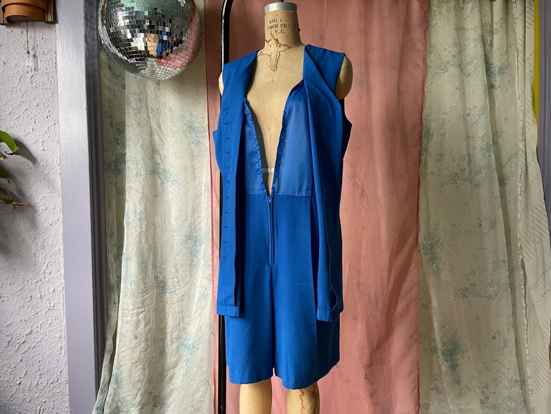 Op de afbeelding: Een koninklijk blauwe, mouwloze jumpsuit met een diepe V-hals en een ritssluiting. De jumpsuit heeft een aansluitend bovenlichaam en wijde pijpen.