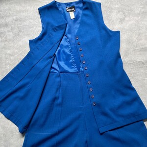 Op de afbeelding: Een koninklijk blauwe, mouwloze vest en bijpassende shorts set met een knoopsluiting. De vest heeft een V-hals en de shorts hebben een rechte pijp.
