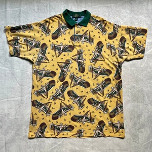 May include: A yellow short-sleeved polo shirt with a green collar and a repeating pattern of brown, green, and white musical instruments.
