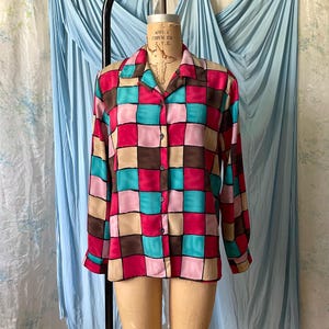 May include: A long-sleeve button-down shirt featuring a vibrant checkered pattern in shades of hot pink, turquoise, brown, and beige. The shirt has a classic collar, a front button placket, and long sleeves with buttoned cuffs, displayed on a mannequin.