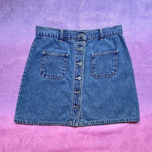 May include: A blue denim skirt with a button front and two pockets. The skirt is a classic style and would be a great addition to any wardrobe.