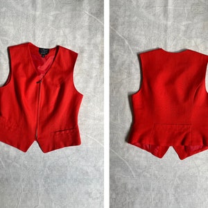 May include: A red sleeveless waistcoat with a zip fastening. The waistcoat has a pointed collar and two pockets.