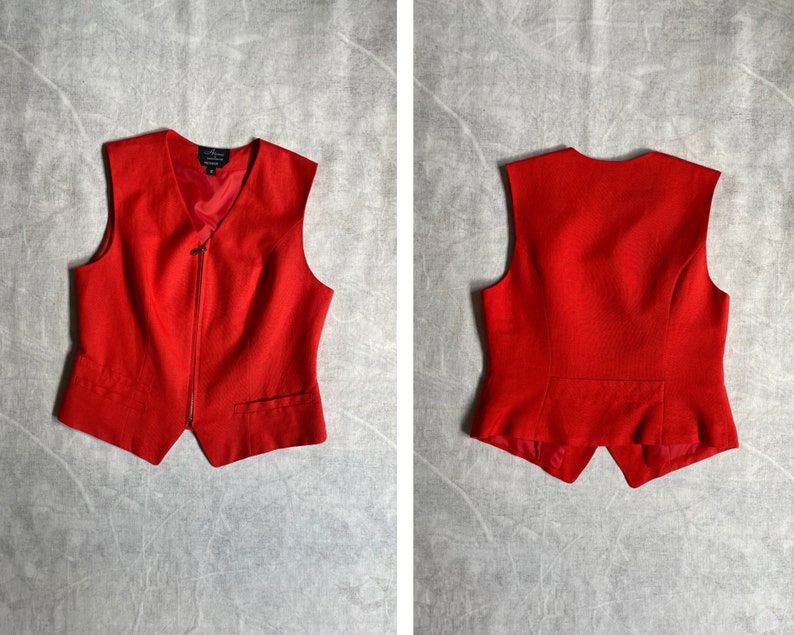 May include: A red sleeveless waistcoat with a zip fastening. The waistcoat has a pointed collar and two pockets.