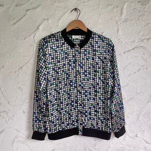 May include: A black and white patterned button-up shirt with green and blue accents. The shirt has a black collar and cuffs and a black zipper closure.