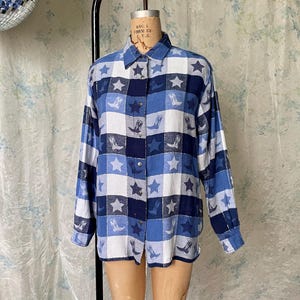 May include: A blue, white, and navy button-down shirt with a plaid pattern. The shirt features star and cowboy boot designs. The long-sleeved shirt is displayed on a mannequin.