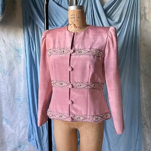 May include: A light pink vintage jacket with long sleeves and a button-up front. The jacket features decorative beading along the neckline, waist, and cuffs. The jacket is displayed on a mannequin.