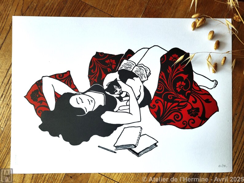 May include: Black and white illustration of a person reclining with a cat and books. The person is lying on a red patterned blanket. Two books and a pencil are on the white surface. The image is signed "Atelier de l'Hermine - Avril 2025".