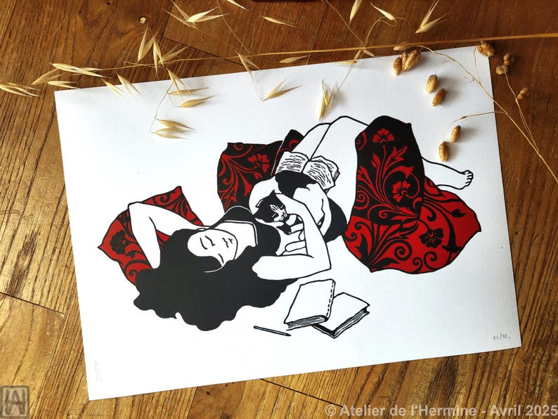 May include: Black and white art print depicting a person reclining with a cat, reading a book. The person is surrounded by a red patterned blanket and pillows. Two notebooks and a pencil are in the foreground.