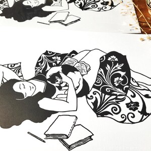 May include: Black and white illustration of a person reclining with a cat, reading a book. The person is surrounded by pillows and a patterned blanket. Two books and a pencil are also visible.