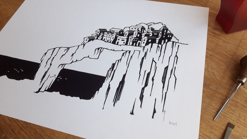 May include: Black and white illustration of a village perched on a cliff overlooking the sea. The village is made up of several buildings with windows and doors. The cliff is tall and rocky, with a large archway in the middle. The sea is dark and choppy.