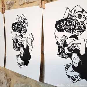 May include: Black and white art prints of a person reclining with a book, featuring long, flowing hair and patterned pillows. The prints are displayed on a clothesline against a stone wall. The artist's signature is visible.