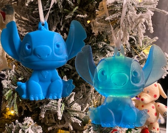 Könnte beinhalten: Zwei blaue Stitch-Weihnachtsbaumschmuckstücke, eines ist einfarbig blau und das andere durchscheinend blau. Beide Schmuckstücke hängen an einem Weihnachtsbaum.