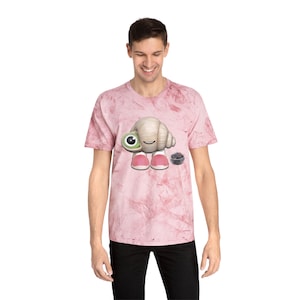 May include: A pink marble-patterned t-shirt featuring a cartoon hermit crab character with a large green eye, pink shoes, and a small basket of berries. The shirt is being worn by a person.