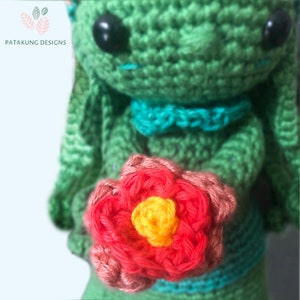 A close-up view of the crochet green Mother Earth doll holding a pink/red flower.