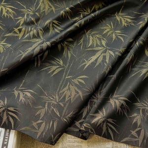 May include: Dark fabric featuring a gold bamboo leaf pattern. The leaves and stalks are in varying shades of gold, creating a textured effect against the dark background. The fabric is draped, showing folds and shadows.