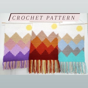 May include: Three crocheted wall hangings with a mountain and sun design. The hangings are in purple, orange, and blue color schemes with fringe at the bottom.