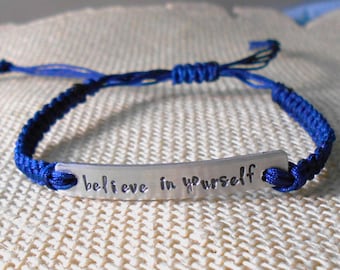 May include: A blue braided bracelet with a silver bar charm that reads "believe in yourself".