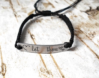 May include: Black cord bracelet with a silver charm that reads "let them" with a heart on each side.