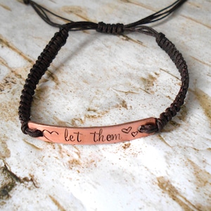 May include: A brown braided cord bracelet with a copper charm that says "let them" with two small hearts on either side.
