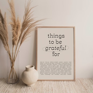 May include: A framed print with a white background and black text that reads "things to be grateful for". The text is in a bold, sans-serif font. The print lists a variety of things to be grateful for, such as fresh air, the sun, ability to breathe, sunsets, concerts, fresh flowers, a roof over your head, to live freely, a cool breeze on a hot summer day, clean water, education, a camera to capture moments, grandparents, freshly cut grass, dogs, board game nights with friends, gooey s'mores by the campfire, baby giggles, sunrises, your favourite movie, taco Tuesdays, mimosas, honey bees, friends who feel like sunshine, chai lattes, thunderstorms, farmers' markets, parents, healthcare, shoes on your feet, mobile transportation, good food, hot sauce, fresh produce, cosy blankets, plants, dinner parties, mobility, birds chirping, toiletries, iced coffee, ice cream, colour, technology, cats, birthdays, fuzzy socks, rainbows.