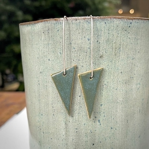 May include: A pair of silver dangle earrings with triangular green ceramic charms. The charms have a light green glaze with a subtle gold sheen.