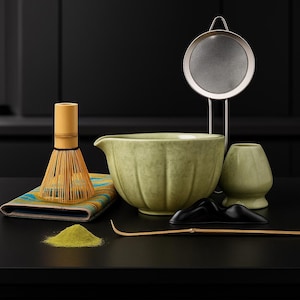 May include: A matcha tea set with a bamboo whisk, a ceramic bowl, a sifter, a tea scoop, and a matcha tea holder. The set includes a small pile of green matcha powder and a colorful patterned cloth.