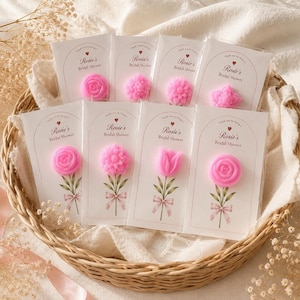 May include: Eight individual clear plastic packages containing pink flower-shaped soaps attached to white cards. Each card features the text 'Thank you for being a part of Rosie's Bridal Shower' with a printed illustration of a green stem and bow.