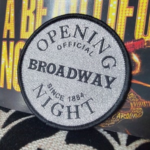 Peut inclure: Un patch circulaire argenté et noir avec le texte "OPENING OFFICIAL BROADWAY NIGHT SINCE 1884".