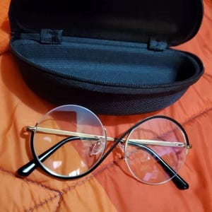 May include: Round, clear, gold-rimmed glasses with black frames and a black carrying case.