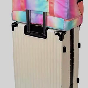 May include: A cream-colored rolling suitcase with a matching tie-dye duffel bag on top. The duffel bag features a rainbow of colors, including pink, blue, and yellow. The suitcase has black accents and wheels, perfect for travel.