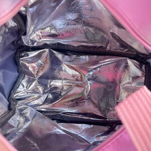 Puede incluir: Bolsa de almuerzo aislante rosa con interior plateado. La bolsa tiene cierre de cremallera y asa rosa. El interior cuenta con un compartimento plateado y aislado para mantener fr&iacute;os los alimentos y bebidas.