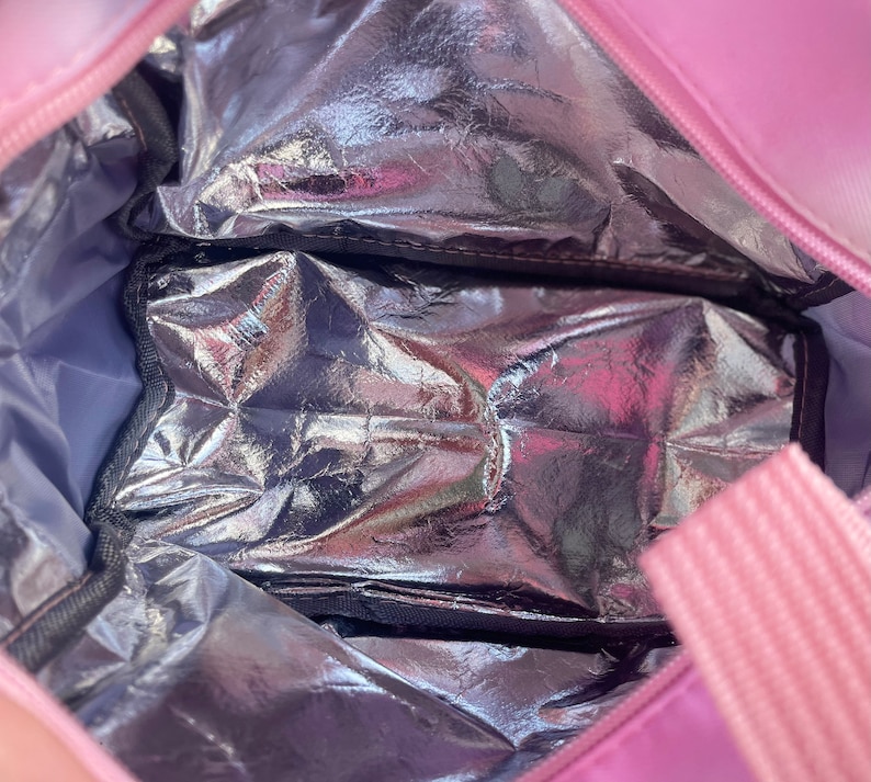 Puede incluir: Bolsa de almuerzo aislante rosa con interior plateado. La bolsa tiene cierre de cremallera y asa rosa. El interior cuenta con un compartimento plateado y aislado para mantener fr&iacute;os los alimentos y bebidas.