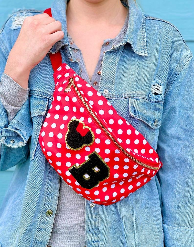 May include: Red fanny pack with white polka dots, a gold zipper, and a red strap. The pack features a black and gold patch of a mouse head and the letter "B".