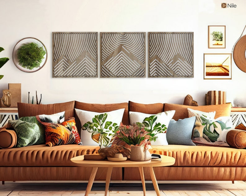 May include: A brown leather sofa with multiple throw pillows in various patterns and colors, including green, orange, and blue. The sofa is in front of a white wall with three wooden wall decor pieces featuring a geometric design.