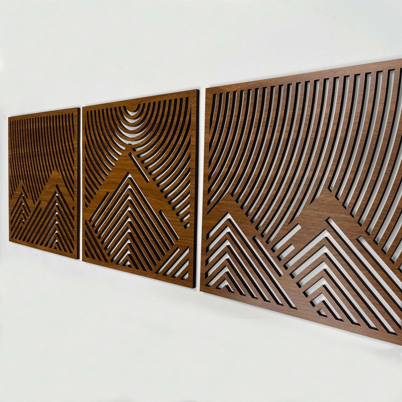 May include: Three wooden wall panels with a geometric mountain design. The panels are made of dark brown wood and have a layered, three-dimensional effect.