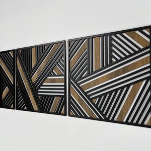 May include: Three black metal wall panels with a geometric pattern of intersecting lines. The panels are layered to create a three-dimensional effect. The background of the panels is a light brown wood.