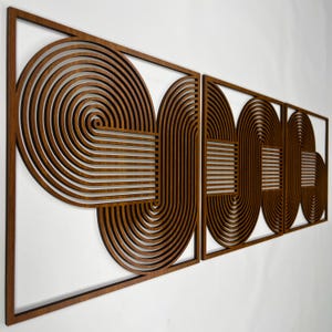 Op de afbeelding: Houten wandkunst met een geometrisch ontwerp. Het kunstwerk bestaat uit vier rechthoekige panelen met een herhalend patroon van gebogen lijnen en vormen. Het hout heeft een warme, bruine tint en het ontwerp staat tegen een witte achtergrond.