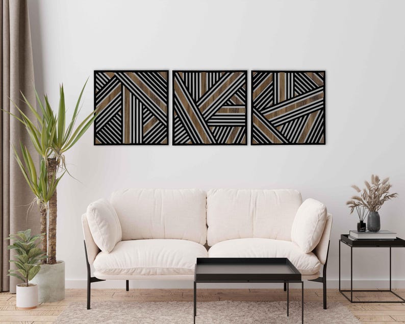 May include: Three black framed wall art pieces with a geometric pattern of brown and white stripes. The art is displayed on a white wall above a white couch and a black coffee table.