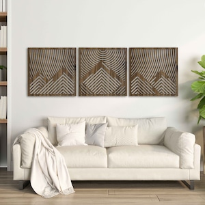 May include: Three wooden wall panels with a geometric design of overlapping triangles and lines. The panels are made of acacia wood and have a natural brown finish.