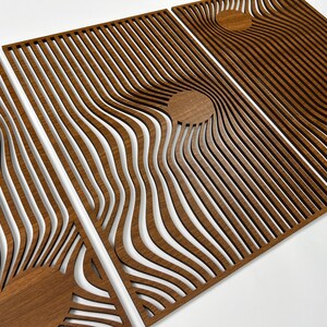 May include: Three wooden panels with a repeating wave pattern and circular accents. The panels are made of a warm brown wood, with the wave pattern creating a sense of depth and movement. The design is modern and abstract.