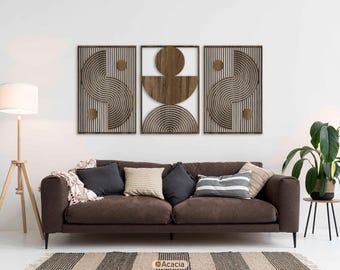 May include: Three wooden wall art panels with geometric designs. The panels feature a combination of curved and straight lines in a natural wood tone, set against a light background. The artwork is framed in dark wood and hangs above a brown sofa.