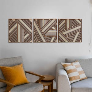 May include: Three wooden wall art panels with a geometric pattern of brown and white stripes. The panels are arranged horizontally and are hung on a white wall.