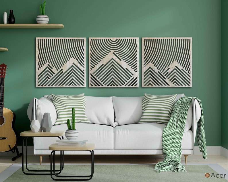 May include: Three wooden wall art panels with a geometric mountain design. The panels are in a light wood tone and feature a pattern of overlapping lines and shapes. The panels are arranged in a row on a green wall above a white sofa.