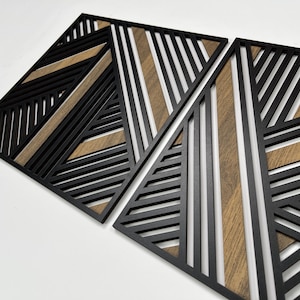 May include: Two black geometric wall decor panels with a wood grain pattern. The panels are made of thin strips of wood that are arranged in a geometric pattern. The panels are designed to be hung on a wall.