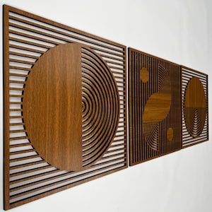 May include: A set of three wooden wall art panels with geometric designs. The panels feature a combination of solid wood and slatted patterns, with circular and semi-circular shapes. The wood has a warm, brown tone, creating a modern and artistic aesthetic.