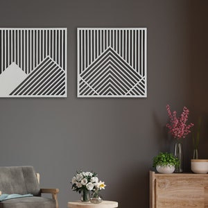 May include: Two white geometric wall art pieces with a black and white striped pattern. The pieces are hanging on a grey wall above a wooden dresser.